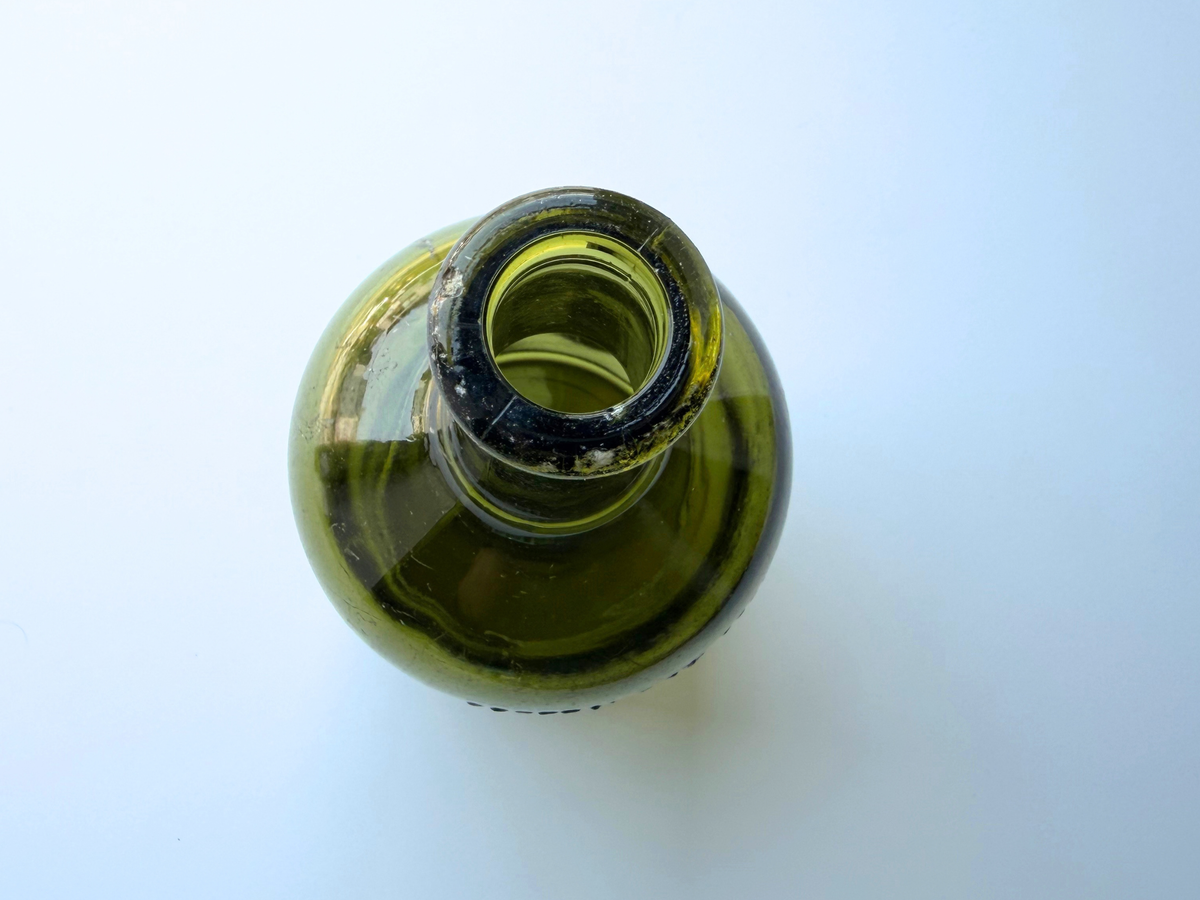 Top-down view into the open mouth of a vintage olive green glass Chivas bottle