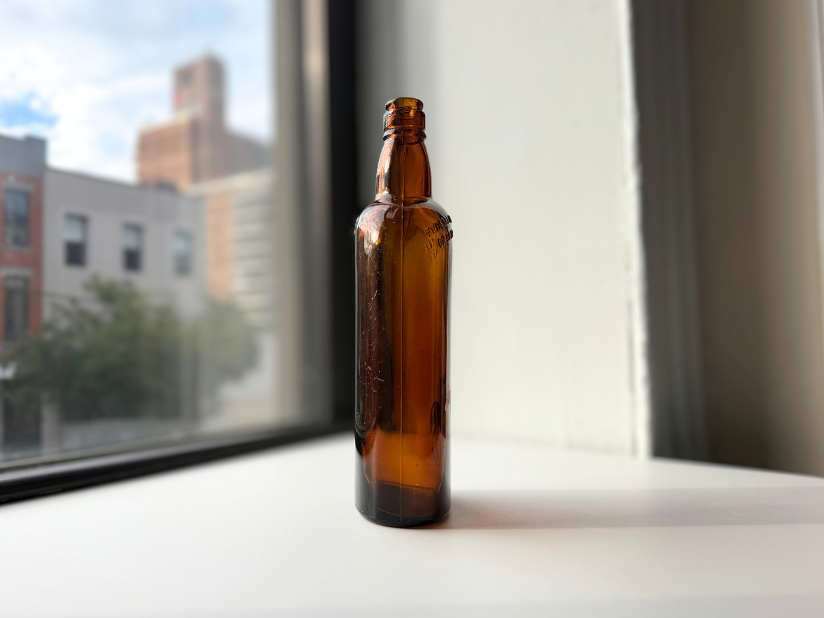 Side profile of the vintage amber White Horse bottle on a windowsill, with embossed shoulder lettering and a few light scratches in the glass.