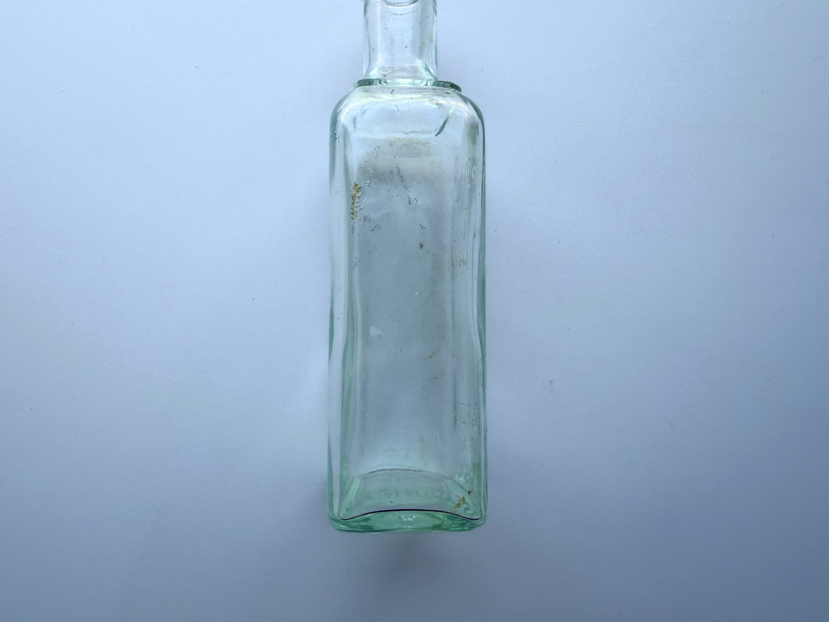 Close view of the side panel of a vintage greenish-blue glass hair dressing bottle