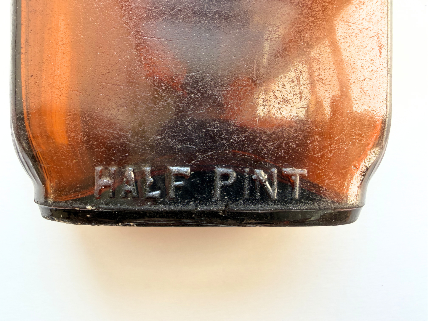 Close-up of HALF PINT embossed into the base of a sea-worn amber glass flask