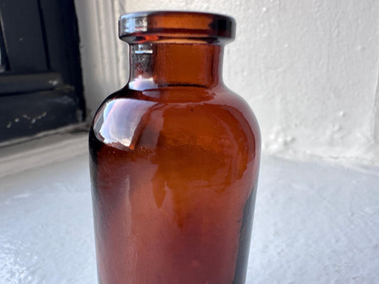 Amber medicine vial side view showing narrow neck and slightly flared base, 1950s pharmaceutical form