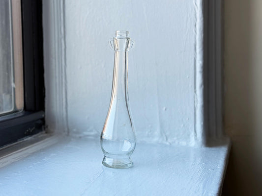 Front view of a vintage Pompeian Olive Oil glass bottle, showcasing its elongated shape and bulbous base on a white windowsill – Brooklyn Sea Glass