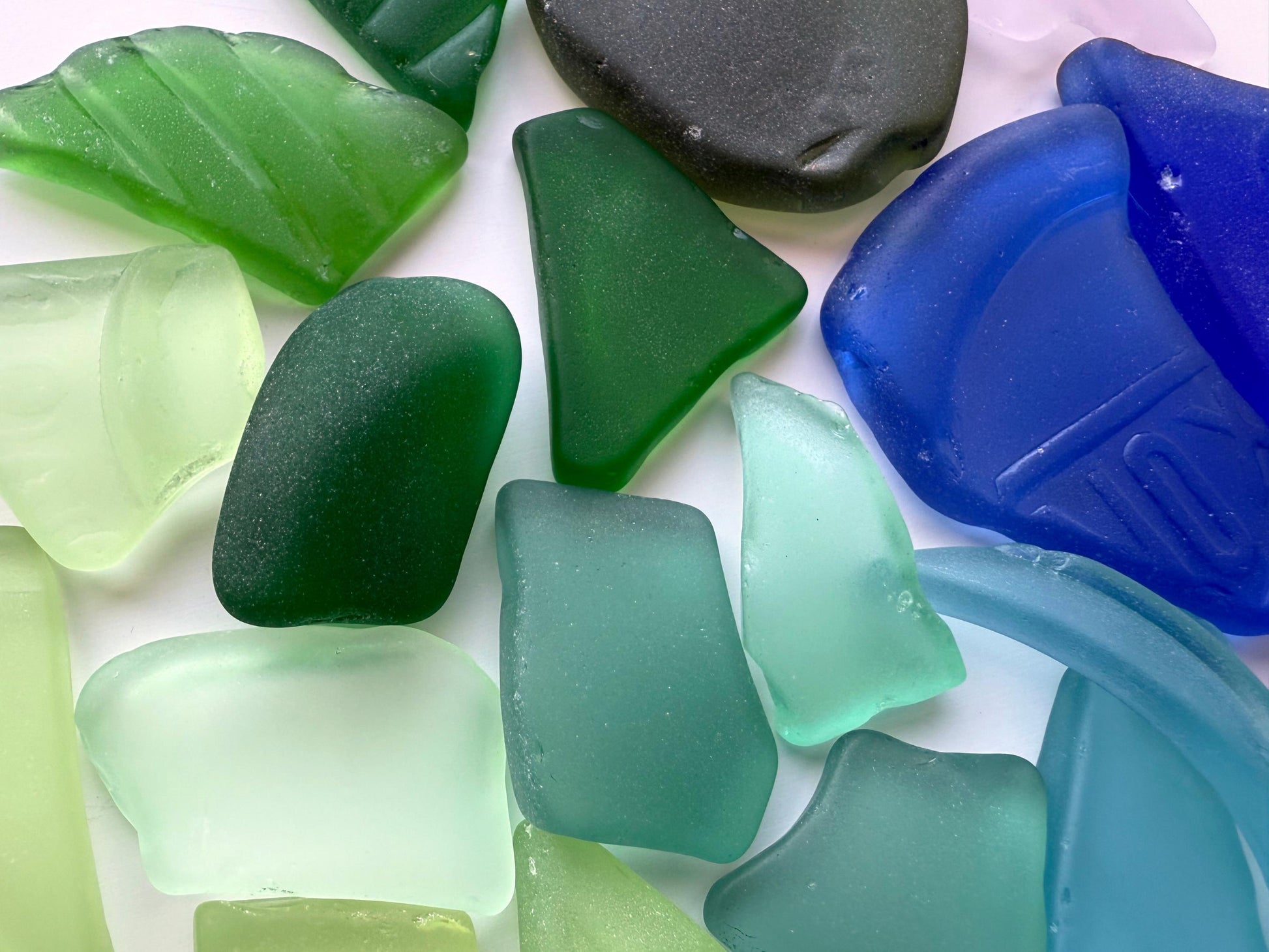 Detailed macro photo of sea glass in soft mint, teal, and emerald. All large pieces are tumbled from antique or vintage glass for smoothness and color clarity. Ideal for statement jewelry, beach decor, or mosaic work. Sustainably made in New York.