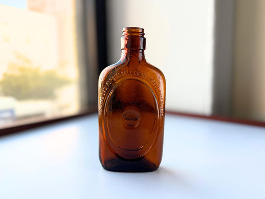 Vintage 1950s amber glass liquor flask 6.75 inches tall with oval embossing and Federal Law prohibition warning. Art Deco oval design, rescued from NYC historic landfills – Brooklyn Sea Glass