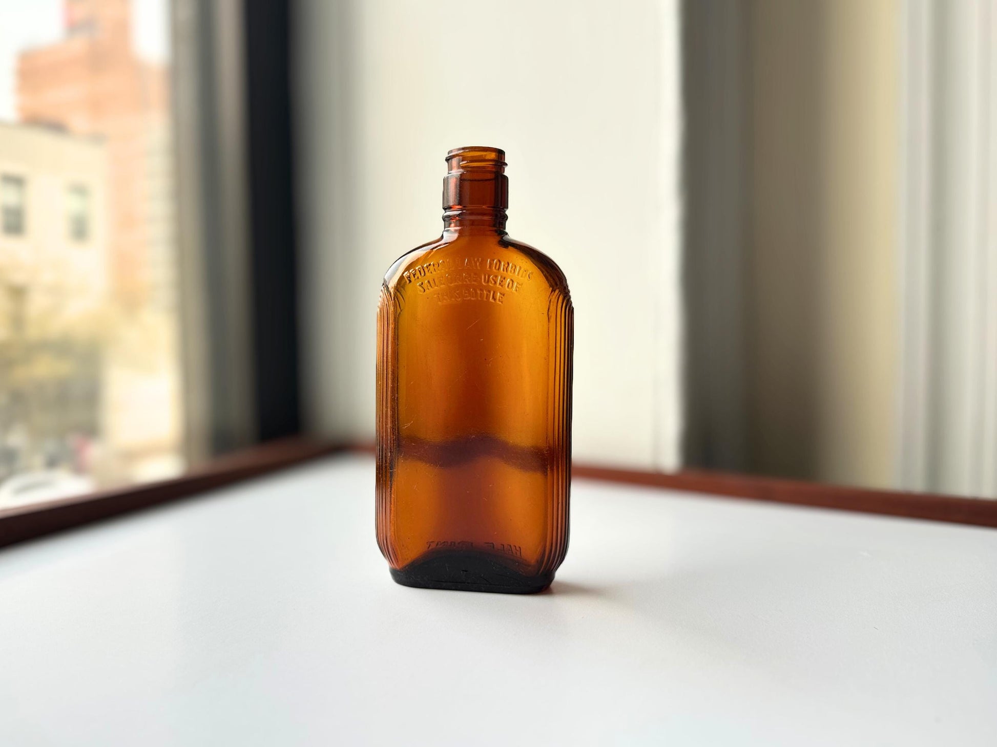 Vintage 1952 mid-century amber glass flask 7.5 inches tall by 3.4 inches wide, rescued from NYC beaches. Ribbed design with embossed Federal Law Forbids Sale Or Reuse Of This Bottle text – Brooklyn Sea Glass