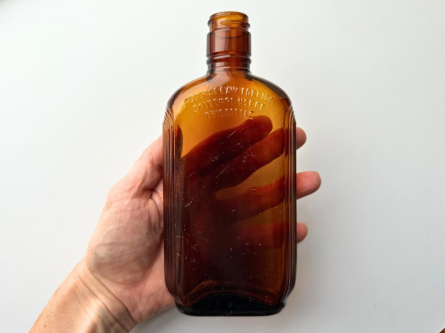 Vintage 1952 mid-century amber glass flask 7.5 inches tall by 3.4 inches wide, rescued from NYC beaches. Ribbed design with embossed Federal Law Forbids Sale Or Reuse Of This Bottle text – Brooklyn Sea Glass