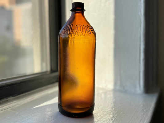 Vintage amber glass Clorox bottle, likely a quart size, with embossed CLOROX text. Ideal for collectors or retro-inspired decor. This collectible bottle is a piece of cleaning history, showing the iconic brand's early packaging design.