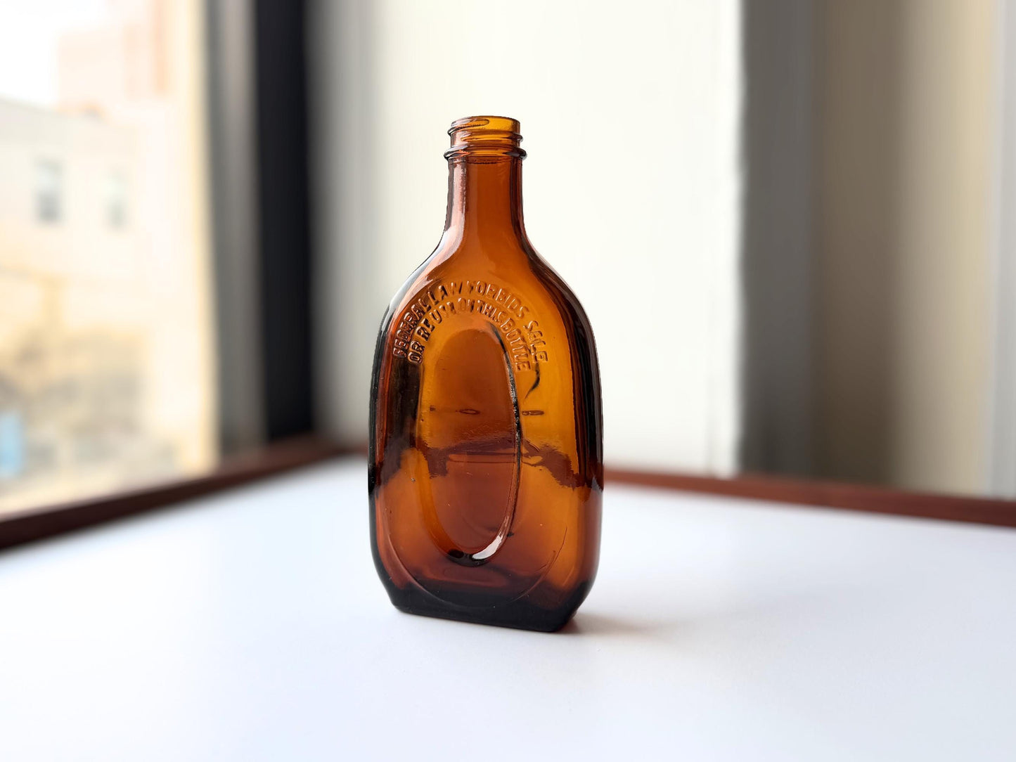 Vintage amber flat scotch bottle 7 inches tall with ornate embossed front design, hand-recovered from NYC mid-century dumping grounds – Brooklyn Sea Glass