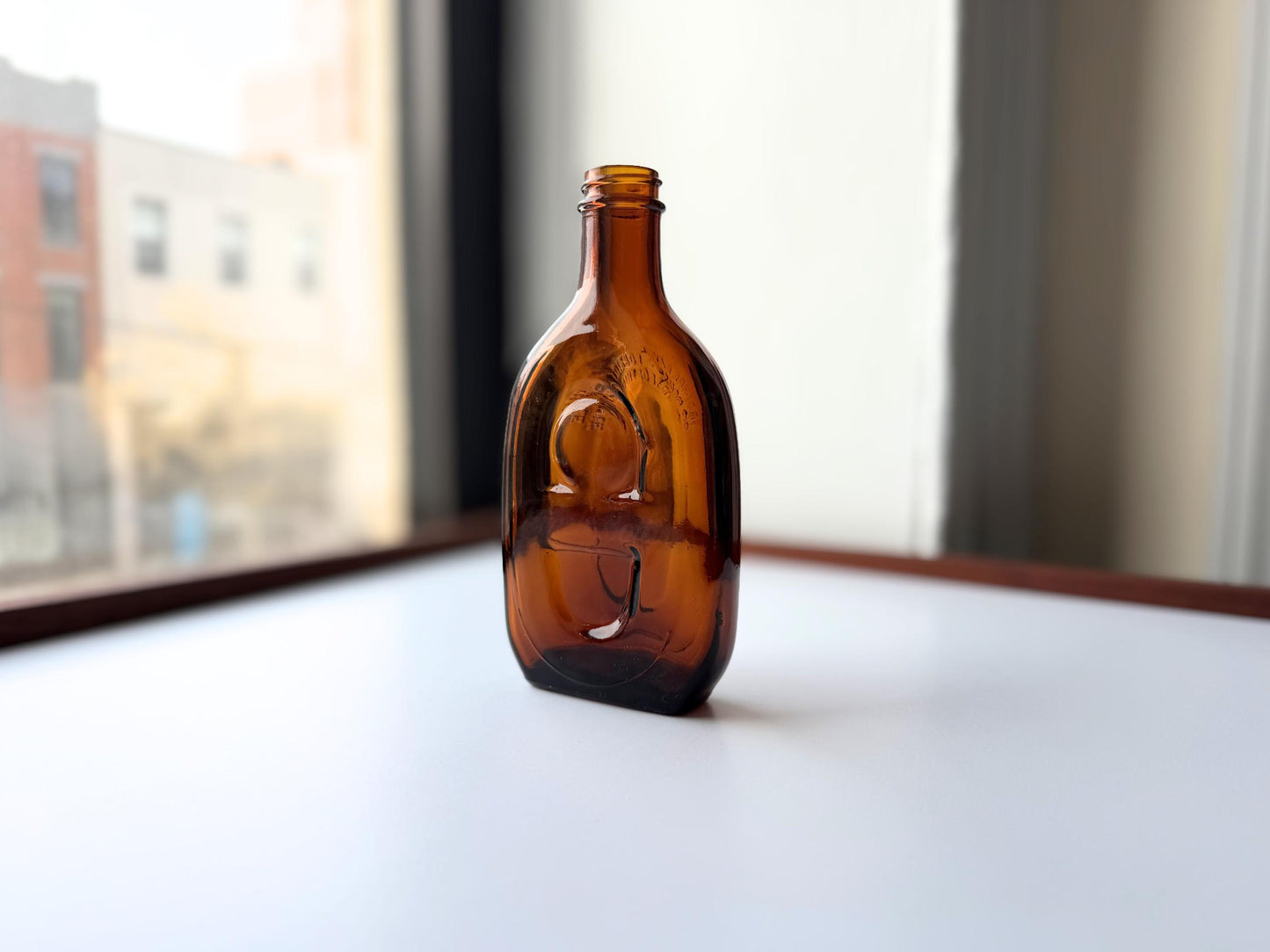 Vintage amber flat scotch bottle 7 inches tall with ornate embossed front design, hand-recovered from NYC mid-century dumping grounds – Brooklyn Sea Glass