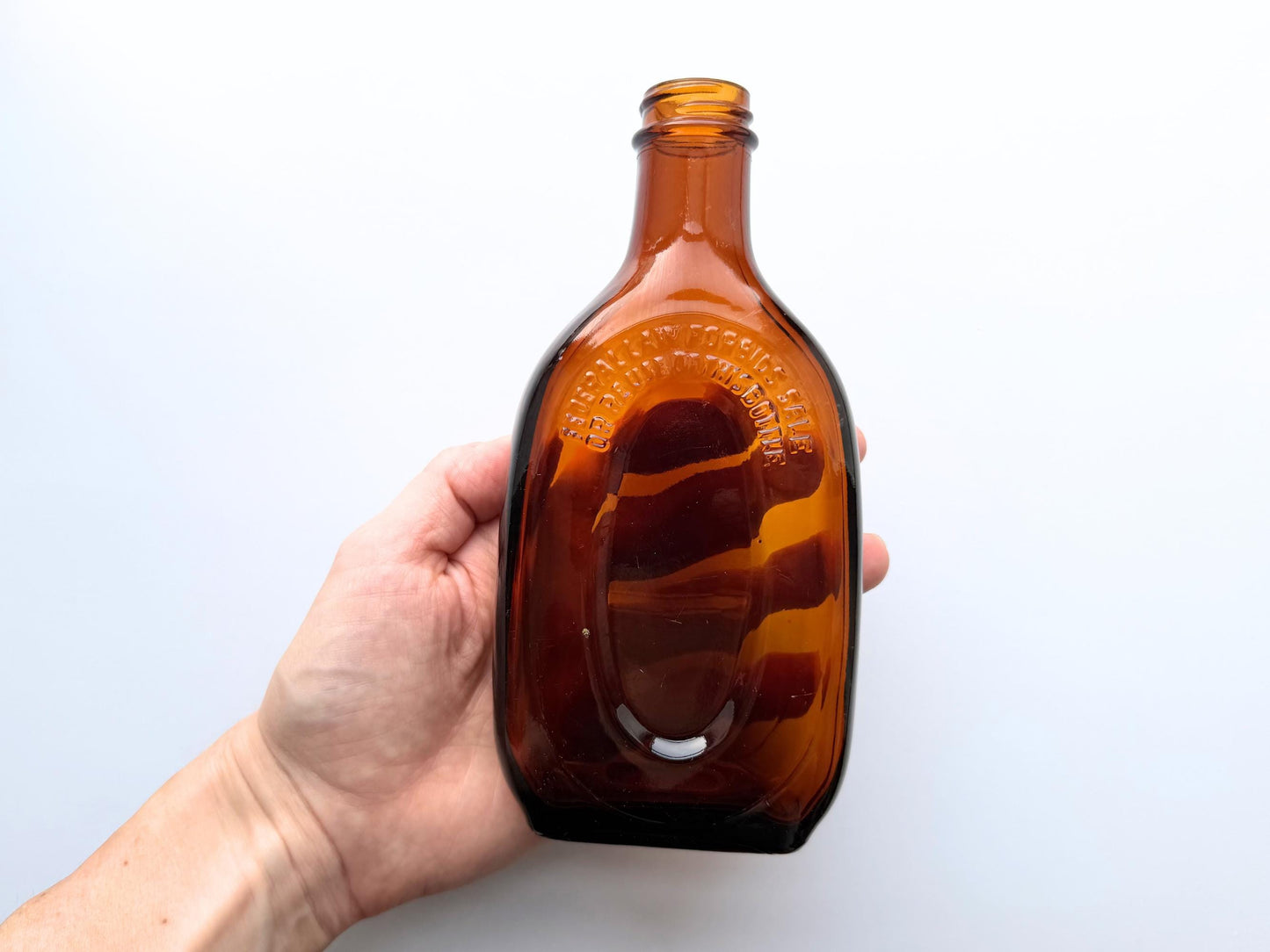 Vintage amber flat scotch bottle 7 inches tall with ornate embossed front design, hand-recovered from NYC mid-century dumping grounds – Brooklyn Sea Glass