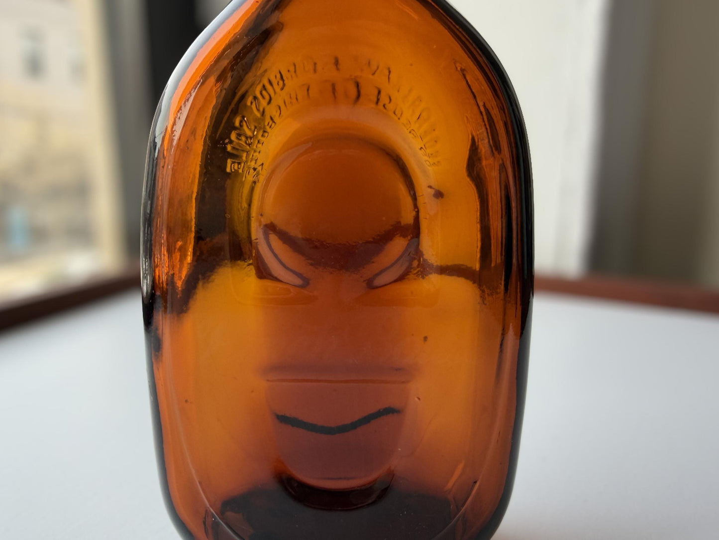 Vintage amber flat scotch bottle 7 inches tall with ornate embossed front design, hand-recovered from NYC mid-century dumping grounds – Brooklyn Sea Glass