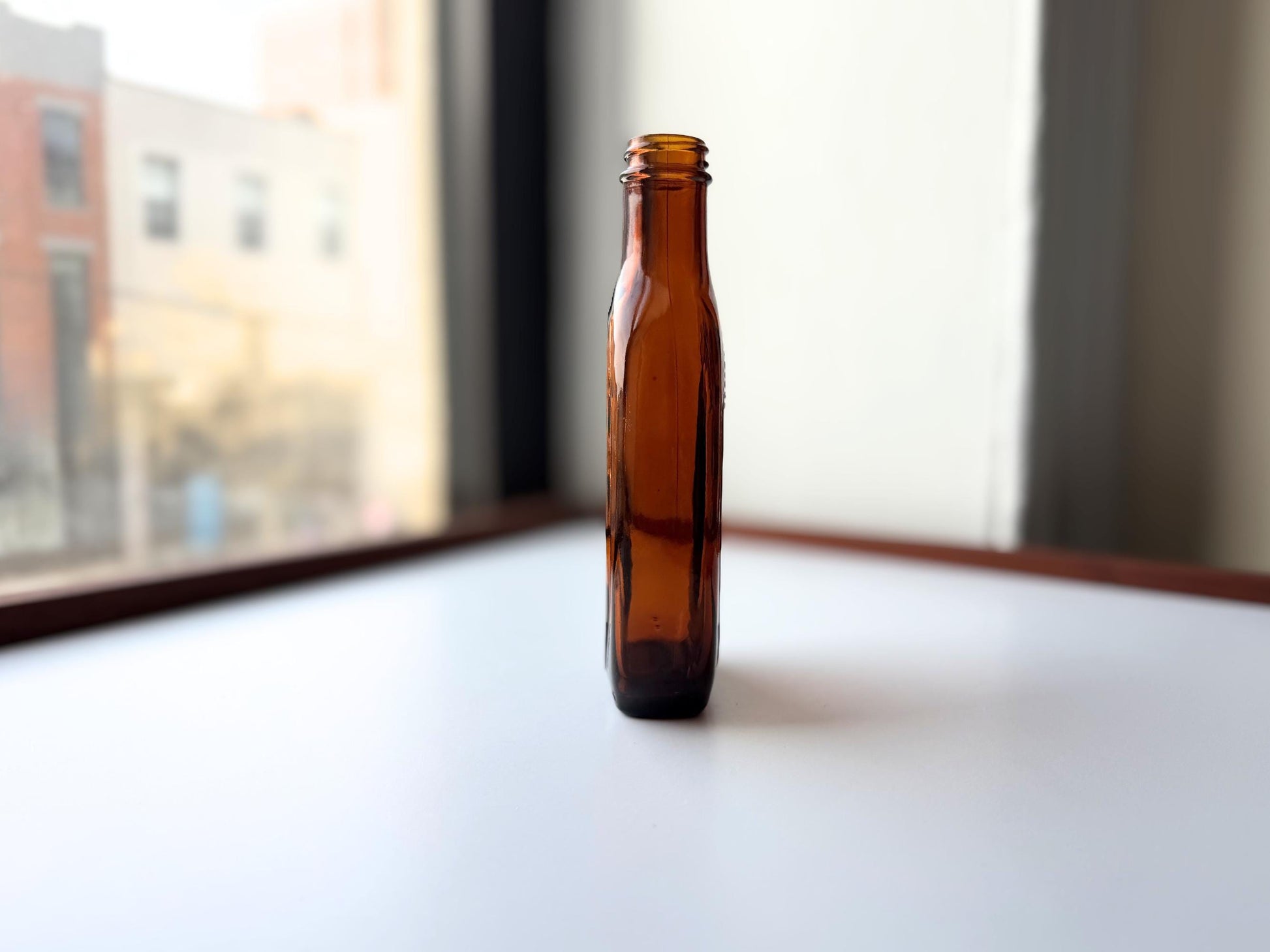 Vintage amber flat scotch bottle 7 inches tall with ornate embossed front design, hand-recovered from NYC mid-century dumping grounds – Brooklyn Sea Glass