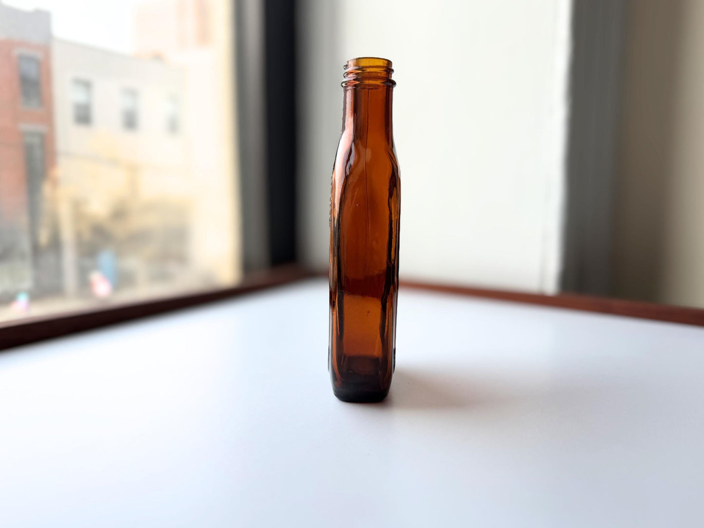 Vintage amber flat scotch bottle 7 inches tall with ornate embossed front design, hand-recovered from NYC mid-century dumping grounds – Brooklyn Sea Glass
