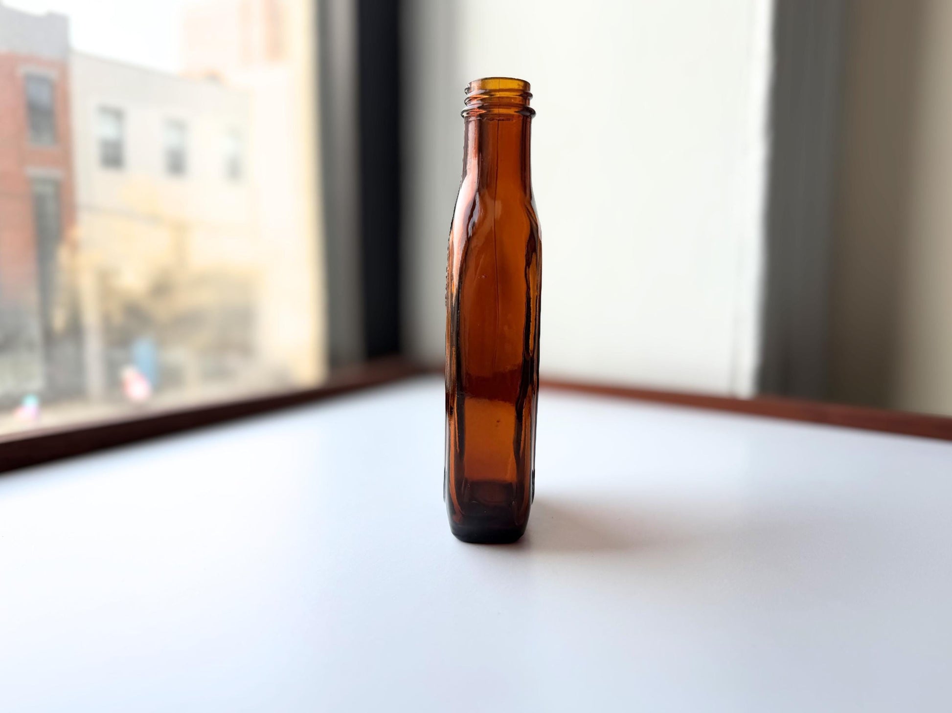 Vintage amber flat scotch bottle 7 inches tall with ornate embossed front design, hand-recovered from NYC mid-century dumping grounds – Brooklyn Sea Glass