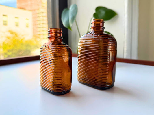 Vintage mid-20th century amber medicine bottle set with distinctive ribbed texture and embossed dosage markings 3oz and 6oz perfect for apothecary displays MCM decor bookshelf styling. Two authentic pharmaceutical bottles feature rich amber glass his