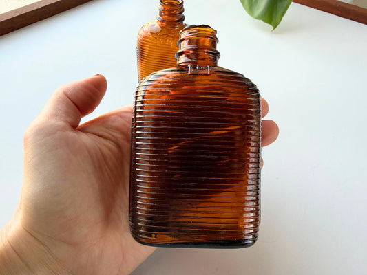 Vintage mid-20th century amber medicine bottle set with distinctive ribbed texture and embossed dosage markings 3oz and 6oz perfect for apothecary displays MCM decor bookshelf styling. Two authentic pharmaceutical bottles feature rich amber glass his