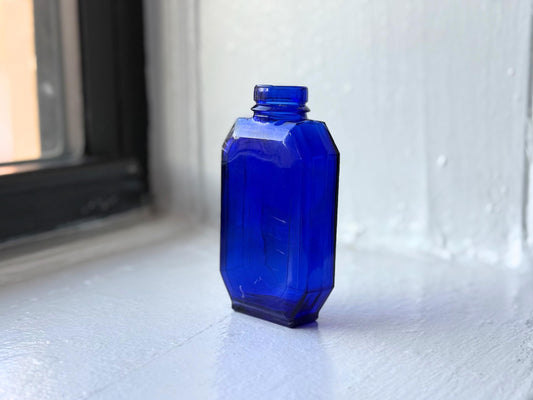 Vintage Evening in Paris cobalt blue glass bottle by Bourjois with faceted Art Deco design, glowing in natural window light – Brooklyn Sea Glass