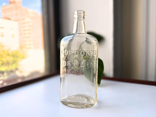 Vintage Gordon's Dry Gin bottle featuring embossed LONDON and ENGLAND text on clear glass. Authentic 9.25-inch tall rectangular liquor bottle rescued from a NYC beach. Perfect for home bar display and vintage spirit collectors.