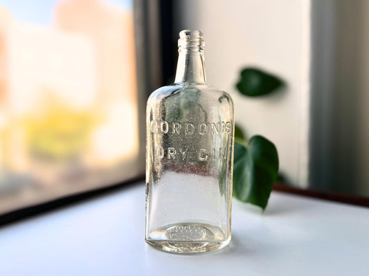 Vintage Gordon's Dry Gin bottle featuring embossed LONDON and ENGLAND text on clear glass. Authentic 9.25-inch tall rectangular liquor bottle rescued from a NYC beach. Perfect for home bar display and vintage spirit collectors.