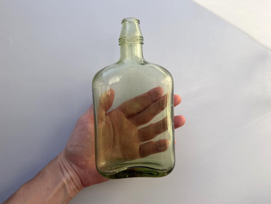 Pale green flask held in hand for scale, 7.5 inch unbranded mid-century green glass spirits form NYC recovery