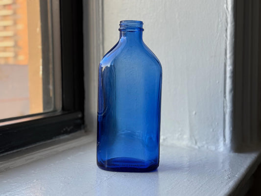 Vintage cobalt blue Phillips Milk of Magnesia bottle displayed on a windowsill glowing in soft natural light – Brooklyn Sea Glass