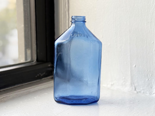Vintage cobalt blue Squibb medicine bottle with rectangular shape and embossed logo glowing in natural light – Brooklyn Sea Glass