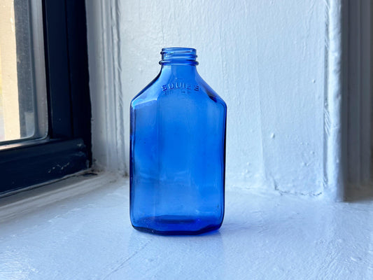 Vintage cobalt blue Squibb glass bottle with octagonal shape displayed against white windowsill – Brooklyn Sea Glass