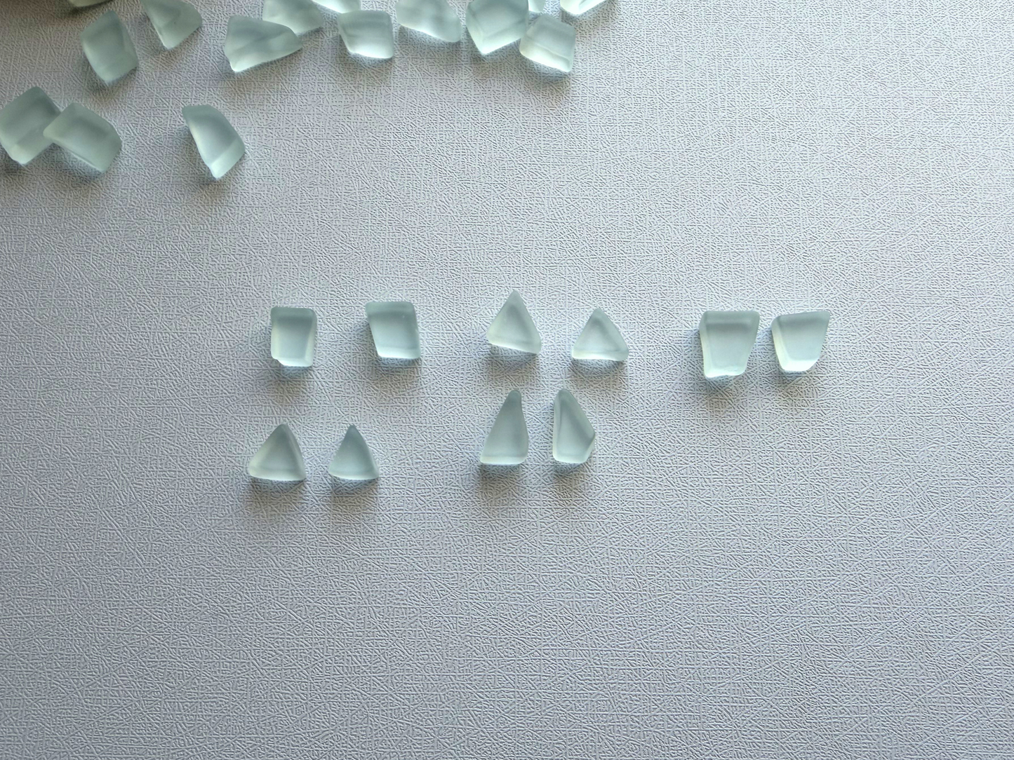 Scattered ice blue vintage glass pieces showing organic geometric shapes and frosted matte finish