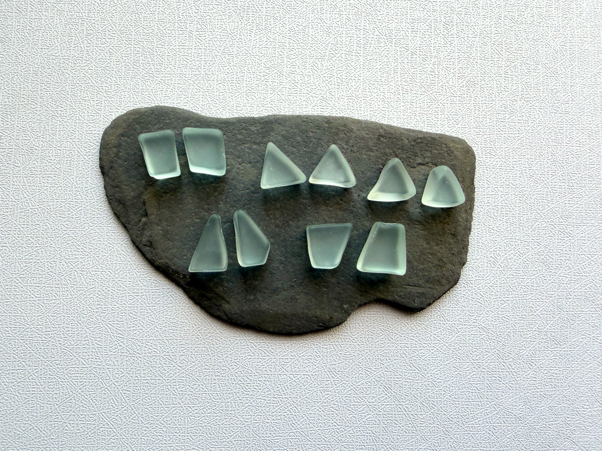 Matched ice blue vintage refrigerator glass pairs for jewelry making, displayed on slate stone