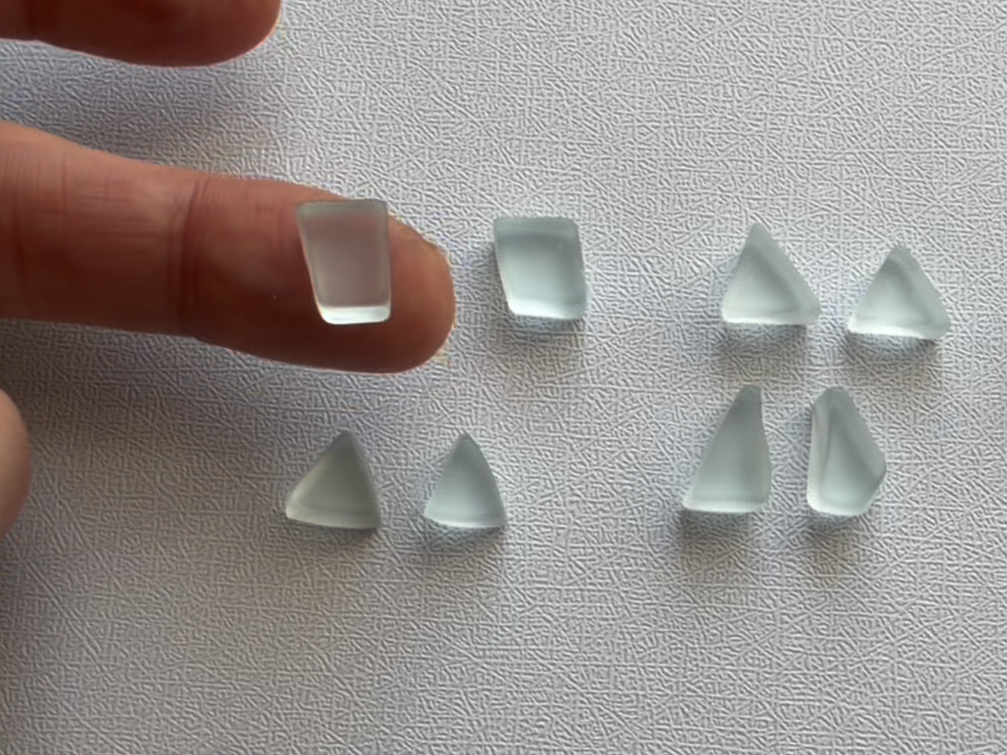 Hand holding a single ice blue glass piece showing scale — approximately 10–15mm for earring making