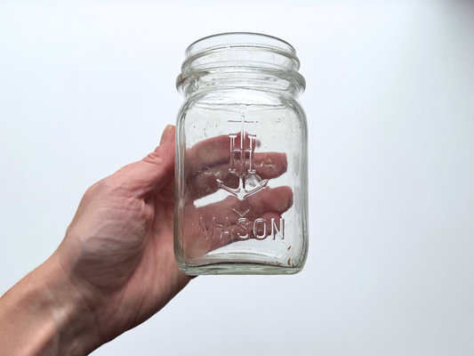 Hand holding an Anchor Hocking mason jar showing the embossed Mason lettering and anchor logo.