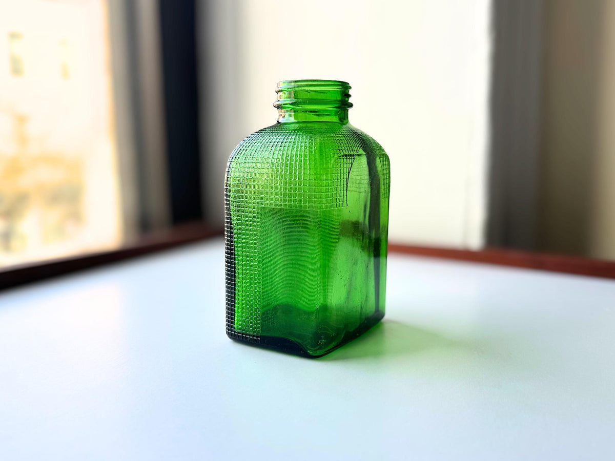 1950 emerald green waffle bottle backlit showing rich green glow and waffle texture in natural window light