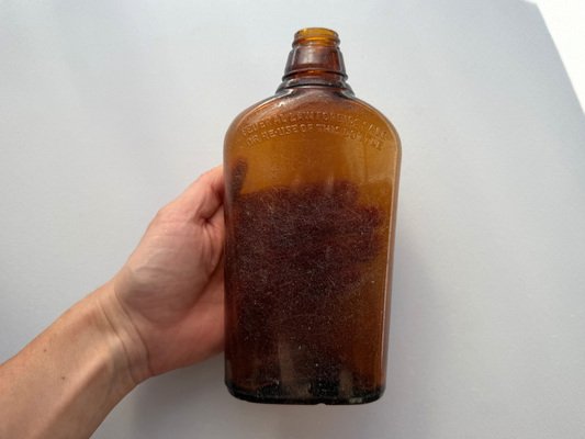 Close-up of Federal Law Forbids Sale embossing on seaworn amber glass flask, frosted matte texture from NYC shoreline