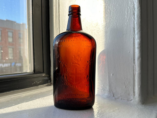 Vintage Hudson Bay Company whiskey bottle with a deep amber hue and a distinctive label featuring a ship and a shield.