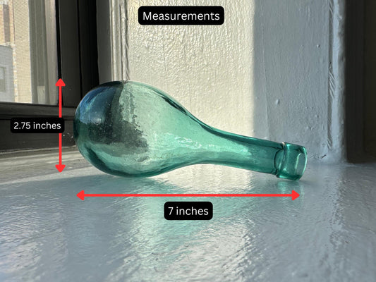 A unique, vintage teal glass bottle with a distinctive shape and a beautiful patina. Perfect for a collector or as a decorative piece. Measures 2.75 inches wide and 7 inches long.