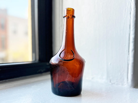 Vintage amber glass bottle with a distinctive embossed design around the central oval label area. The bottle has a dark brown glass.