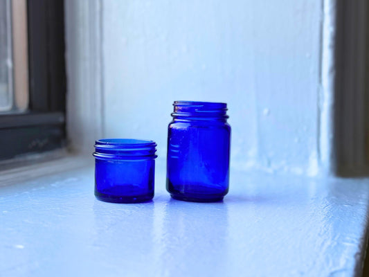Set of two vintage cobalt blue glass jars sitting on a windowsill, showcasing their deep blue color and elegant design.