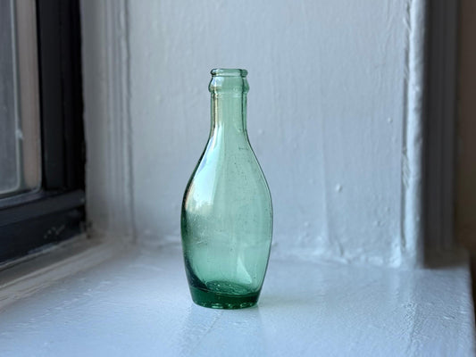 Rear view of the green Perrier glass bottle on a white windowsill, showcasing its minimalist design and vintage details.