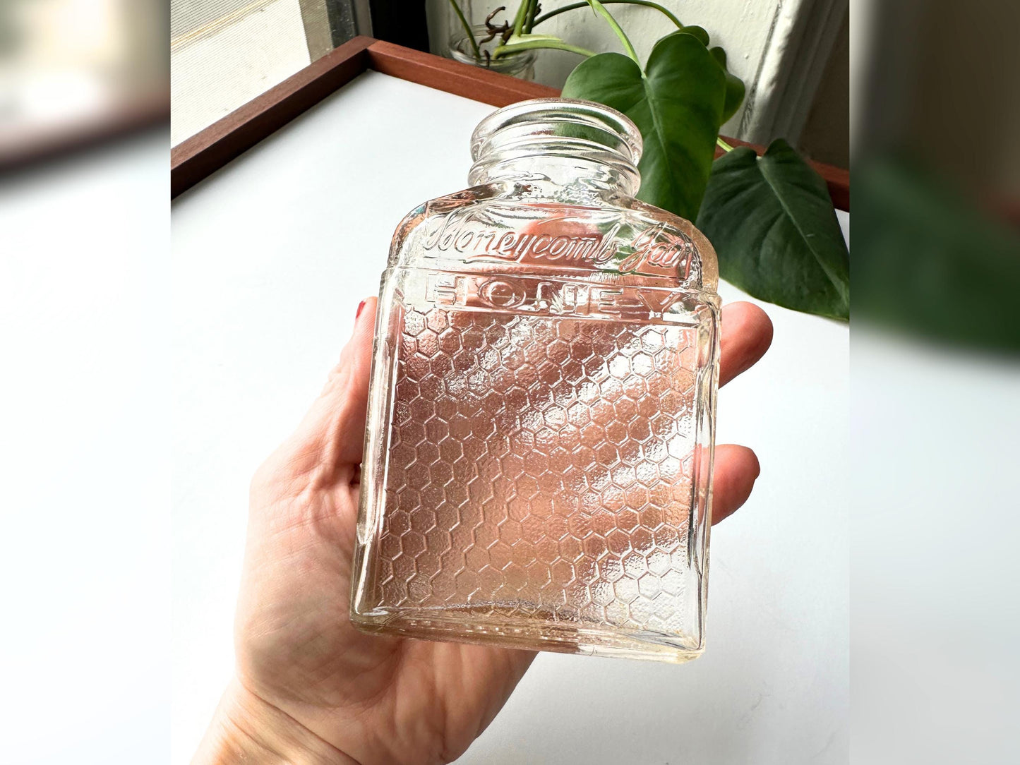 A vintage Lake Shore Honey jar shown held in hand for scale, emphasizing its compact 4.75-inch height and sturdy rectangular form. The embossed “HONEYCOMB JAR” lettering and honeycomb-textured sides are clearly visible. The slight pink tint in the clear glass adds warmth. This image showcases its versatility for display, small-space styling, or functional reuse in rustic kitchens and sustainably designed interiors.