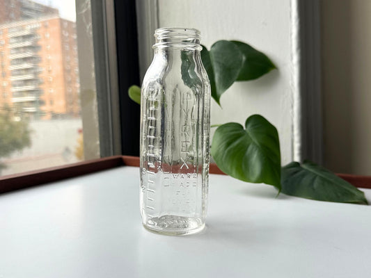 Vintage 1950s Pyrex Evenflo baby bottle in clear glass with embossed measurements and branding, 6.5 inches tall. Mid-century nursery decor perfect for cottagecore or farmhouse styling. Use as minimalist bud vase for dried flowers or display on shelf. Rescued sustainable vintage glassware from Brooklyn Sea Glass. American-made post-war era baby bottle ideal for gender-neutral nursery, baby shower gift, or vintage collector. Embossed text shows Pyrex quality craftsmanship and nostalgic design.