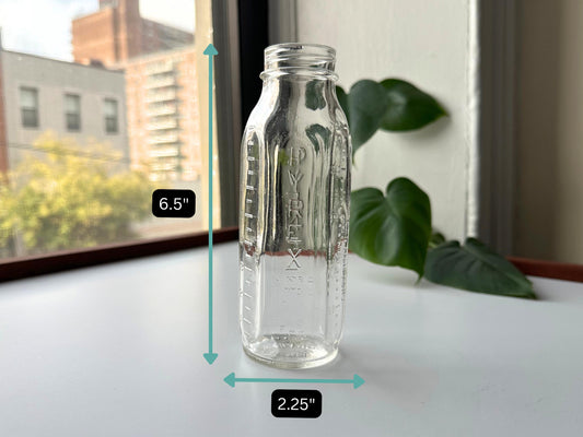 Vintage 1950s Pyrex Evenflo baby bottle with dimension overlay showing 6.5 inches tall by 2.25 inches wide. Clear glass mid-century nursery decor with embossed Pyrex branding and measurements. Rescued sustainable vintage glassware from Brooklyn Sea Glass. Perfect size for minimalist bud vase, cottagecore shelf display, or farmhouse decor. American-made post-war baby bottle ideal for gender-neutral nursery styling, baby shower gifts, or vintage collectors. Heat-resistant Pyrex quality glass.