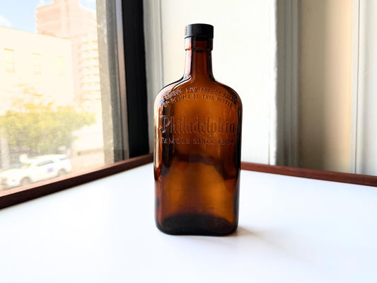 Vintage 1950 Philadelphia whiskey bottle in rich amber glass with embossed Famous Since 1894 lettering and Federal Law prohibition text, perfect for vintage bar cart decor, whiskey collector displays, rustic home bar styling, speakeasy aesthetic, antique spirits collection, rescued from NYC for sustainable eco-friendly home decor