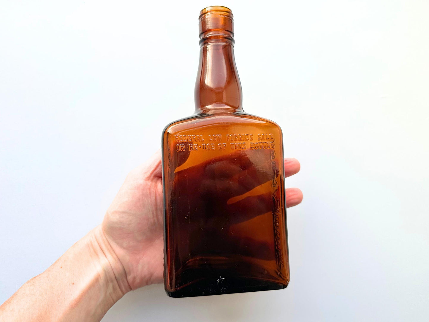 Vintage Mount Vernon straight whiskey bottle, 8.5 inches tall by 3.5 inches wide, rescued from NYC beaches. Features embossed "MOUNT VERNON" lettering and "FEDERAL LAW FORBIDS SALE OR REUSE OF THIS BOTTLE" text authentic to mid-century American spirits bottles. Base marked "ONE PINT" for capacity. Perfect for farmhouse decor, vintage bar cart styling, cottagecore displays, or as unique bud vase. Authentic dug bottle with age-appropriate patina from Brooklyn Sea Glass.