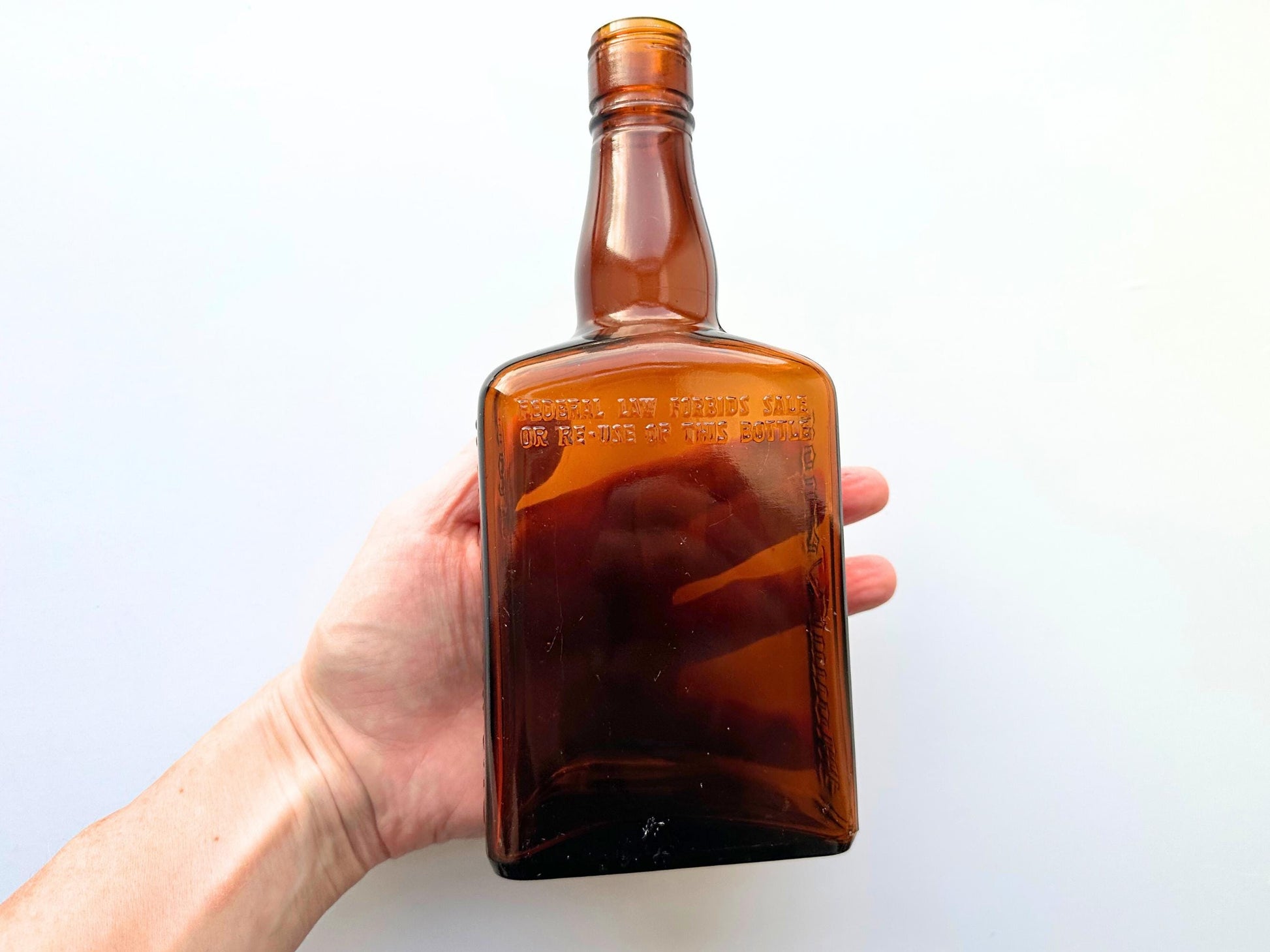 Vintage Mount Vernon straight whiskey bottle, 8.5 inches tall by 3.5 inches wide, rescued from NYC beaches. Features embossed "MOUNT VERNON" lettering and "FEDERAL LAW FORBIDS SALE OR REUSE OF THIS BOTTLE" text authentic to mid-century American spirits bottles. Base marked "ONE PINT" for capacity. Perfect for farmhouse decor, vintage bar cart styling, cottagecore displays, or as unique bud vase. Authentic dug bottle with age-appropriate patina from Brooklyn Sea Glass.
