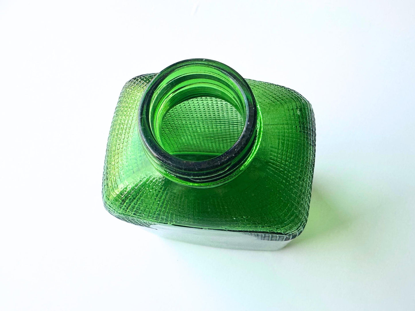 Stunning vintage emerald green glass bottle with distinctive waffle-grid texture throughout perfect for mid-century collectors farmhouse decor. Authentic 1950 bottle features tactile raised square pattern squared flask shape catches light beautifully. Rich emerald green three-dimensional textured surface. Ideal for windowsill displays vintage bottle collections retro kitchen shelves small bud vases statement pieces open shelving MCM cottagecore maximalist vintage interiors sustainable.