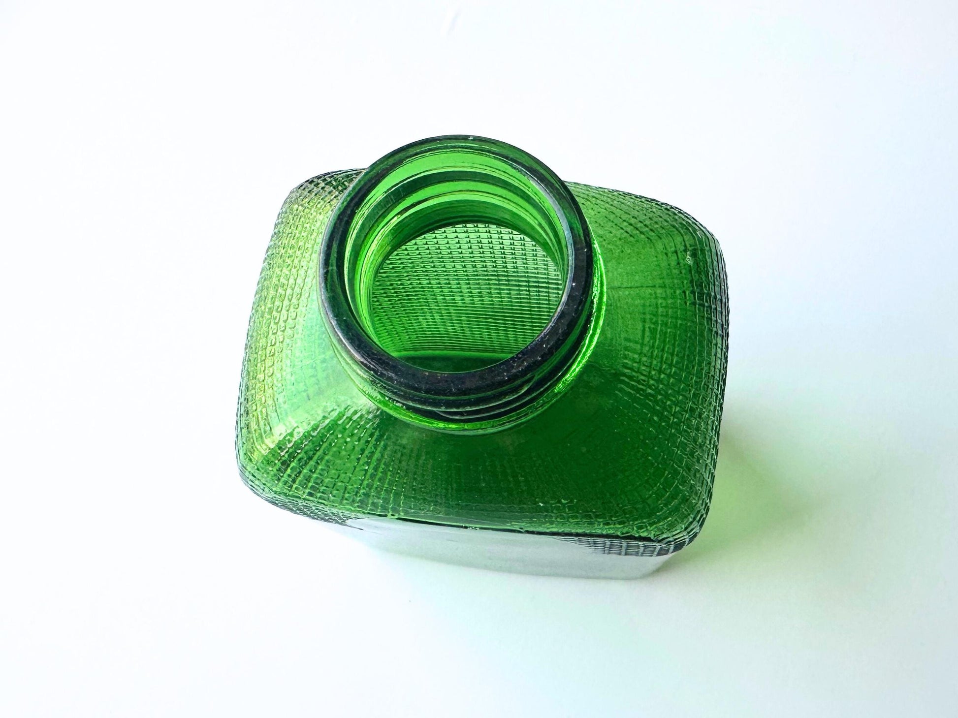 Stunning vintage emerald green glass bottle with distinctive waffle-grid texture throughout perfect for mid-century collectors farmhouse decor. Authentic 1950 bottle features tactile raised square pattern squared flask shape catches light beautifully. Rich emerald green three-dimensional textured surface. Ideal for windowsill displays vintage bottle collections retro kitchen shelves small bud vases statement pieces open shelving MCM cottagecore maximalist vintage interiors sustainable.