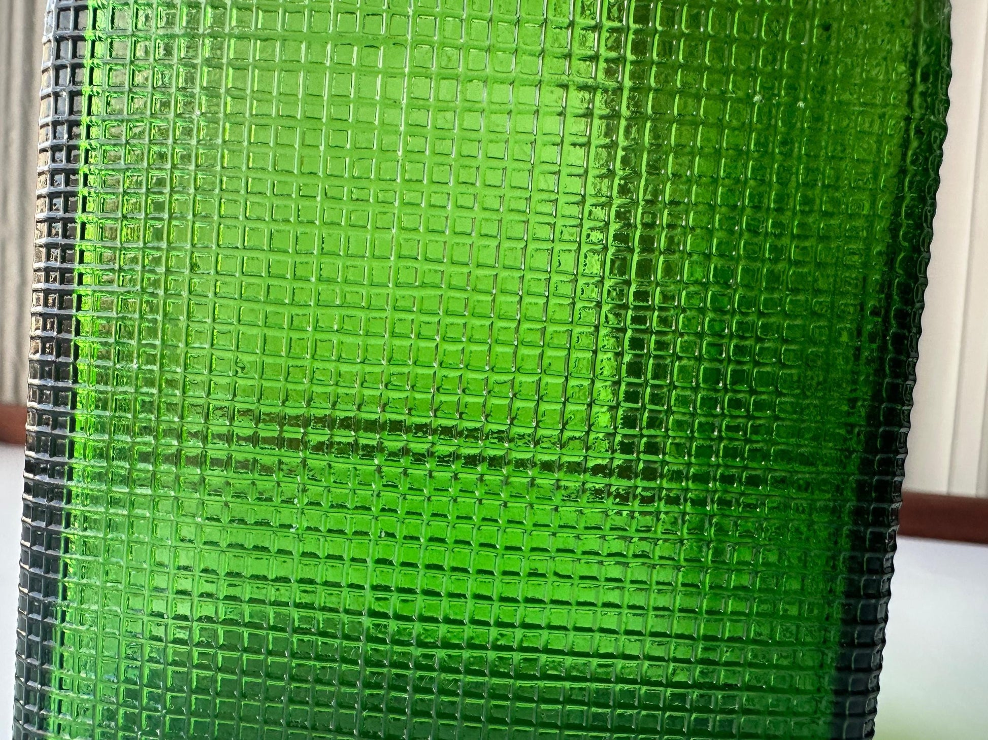 Stunning vintage emerald green glass bottle with distinctive waffle-grid texture throughout perfect for mid-century collectors farmhouse decor. Authentic 1950 bottle features tactile raised square pattern squared flask shape catches light beautifully. Rich emerald green three-dimensional textured surface. Ideal for windowsill displays vintage bottle collections retro kitchen shelves small bud vases statement pieces open shelving MCM cottagecore maximalist vintage interiors sustainable.