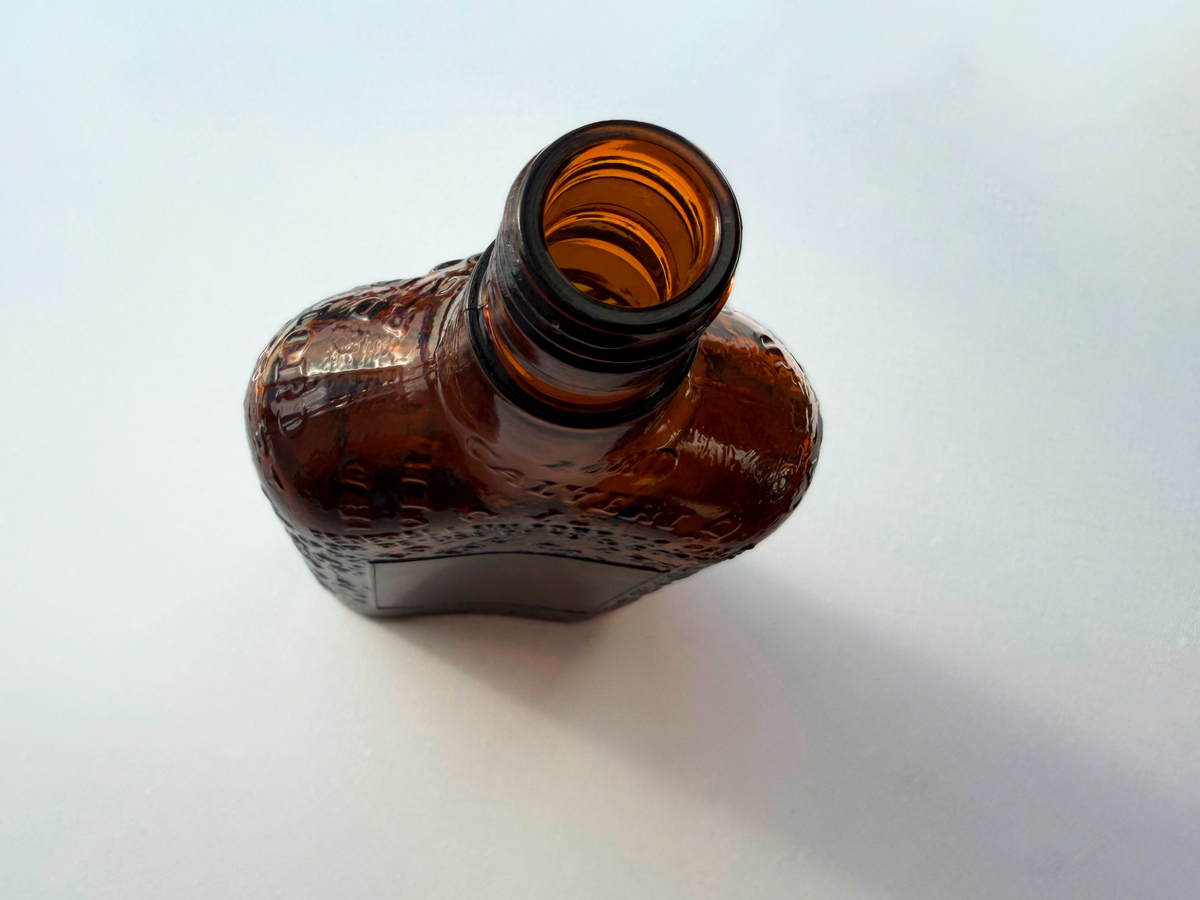 Lord Calvert 1952 amber whiskey flask full front view by window, embossed glass mid-century spirits collectible