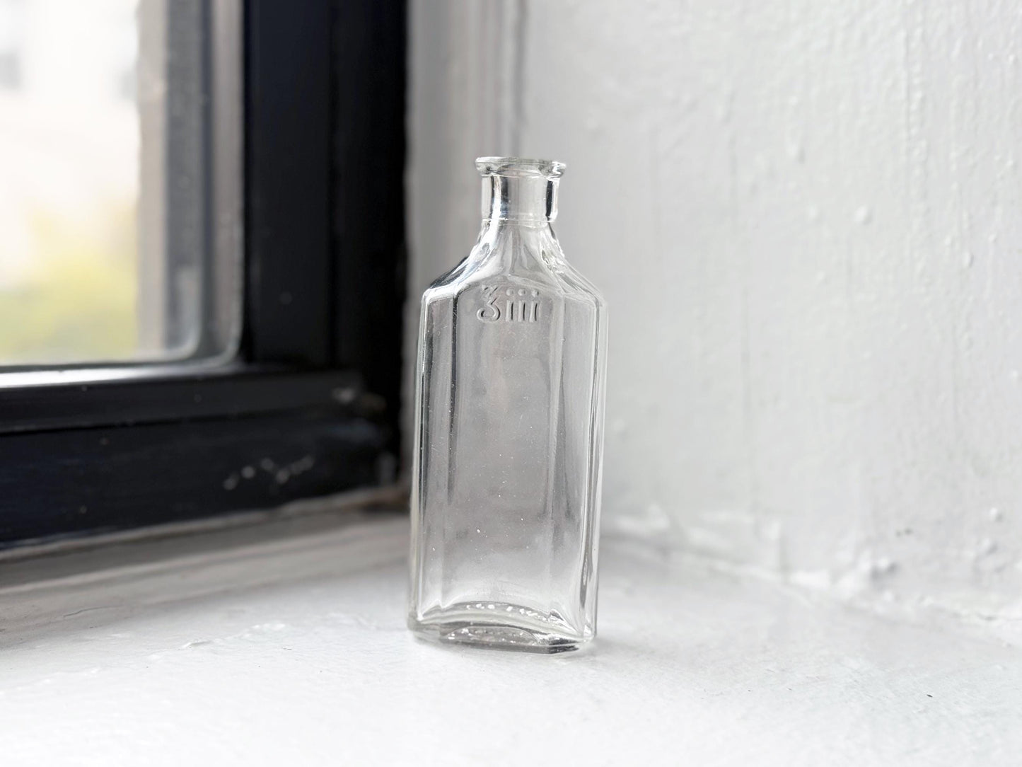 Owens Glass medicine bottle standing upright by window, clear glass apothecary display piece NYC