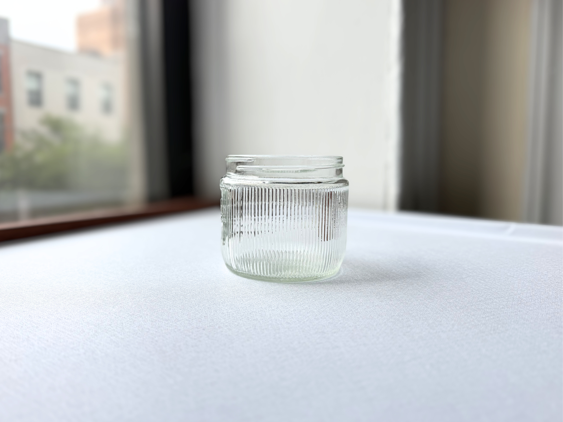 Vintage clear glass Burma-Shave jar with ribbed texture, shown at a three-quarter angle highlighting its Burma-Vita Company branding and textured surface.